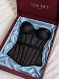 A black sheer mesh and satin underwire corset displayed inside an open dark red LOMIQUE Consoles gift box lined with light blue satin.