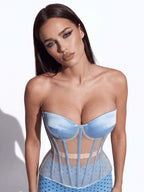 A woman modeling a light blue strapless corset-style top with sheer mesh panels and vertical boning, photographed against a plain white studio background.